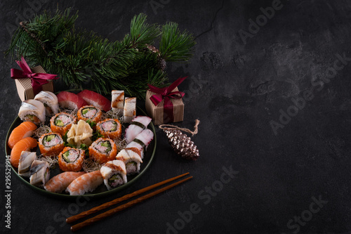 Assorted sushi sashimi set with salmon, tuna and eel on dark slate background with decorations. Christmas or New Year background. Tree branch with gifts. Traditional japanese food. Copy space for text