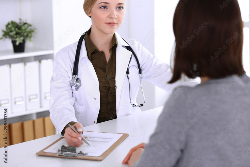 Young woman doctor and patient at medical examination in hospital office. Khaki colored blouse of therapist looks good. Medicine, healthcare and doctor's appointment concept Young woman doctor and patient at medical examination in hospital office. Khaki colored blouse of therapist looks good. Medicine, healthcare and doctor's appointment concept