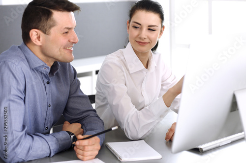 Cheerful smiling businessman and woman working with computer in modern office. Headshot at meeting or workplace. Teamwork, partnership and business concept