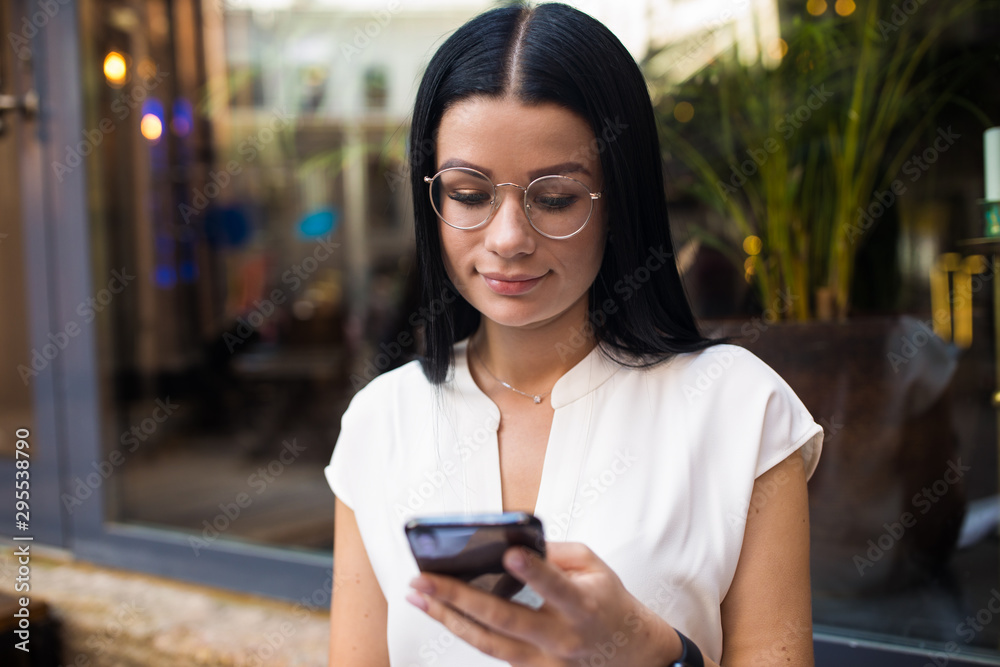 Charming dark hair woman in trendy glasses online shopping store via mobile phone during recreation time. Hipster girl in glasses using apps on cellphone Charming dark hair woman in trendy glasses online shopping store via mobile phone during recreation time. Hipster girl in glasses using apps on cellphone