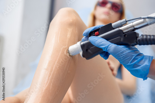 Cosmetology Service. Young woman at beauty clinic lying while doctor removing hair with dynamic laser device close-up