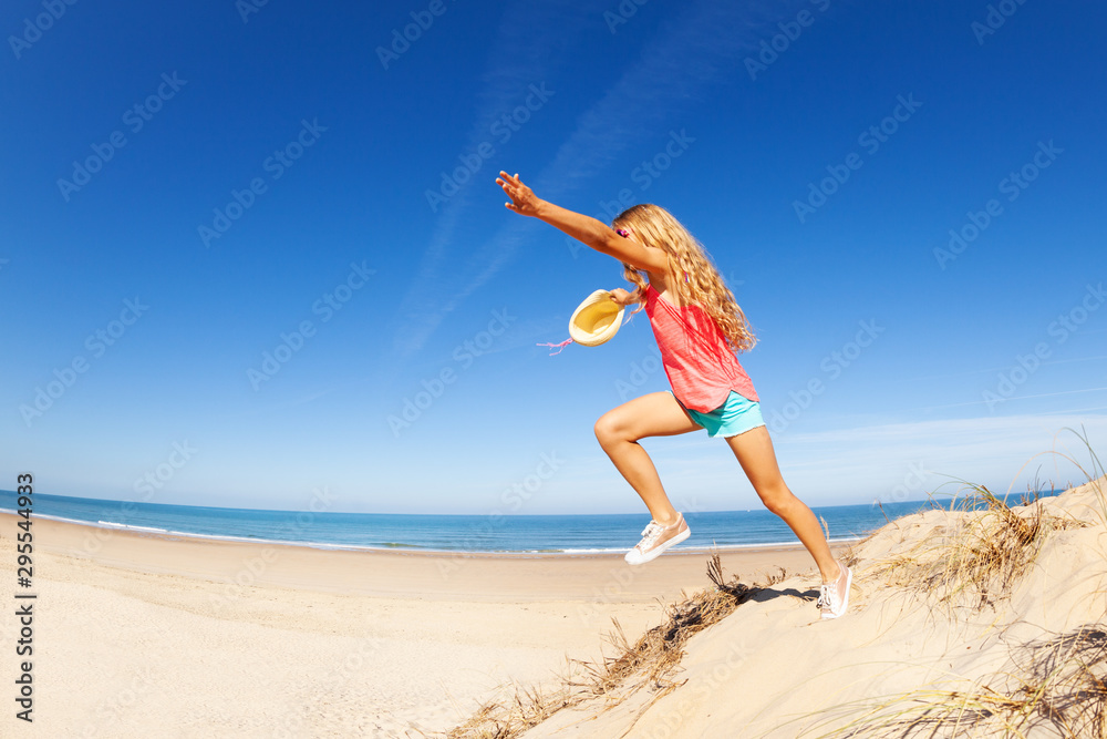 Profile view of girl jump from sand dune over sea Profile view of girl jump from sand dune over sea