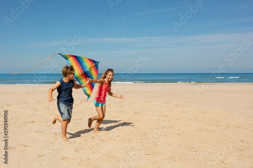 Two kids boy and girl run with color kite on beach