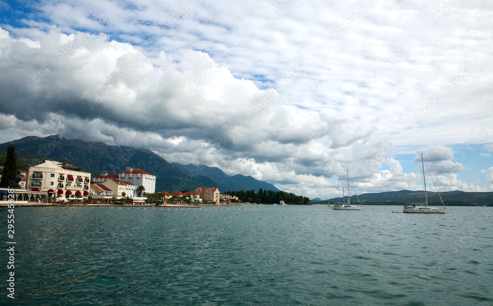 Fototapeta premium Bay in seaside town with boats, houses in green mountains on blue sky,.Tivat, Montenegro