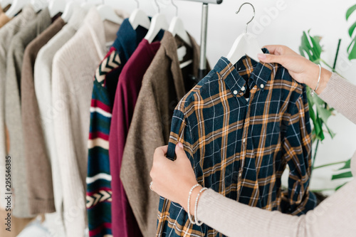 Young female shopper holding hanger with checkered shirt while choosing clothes