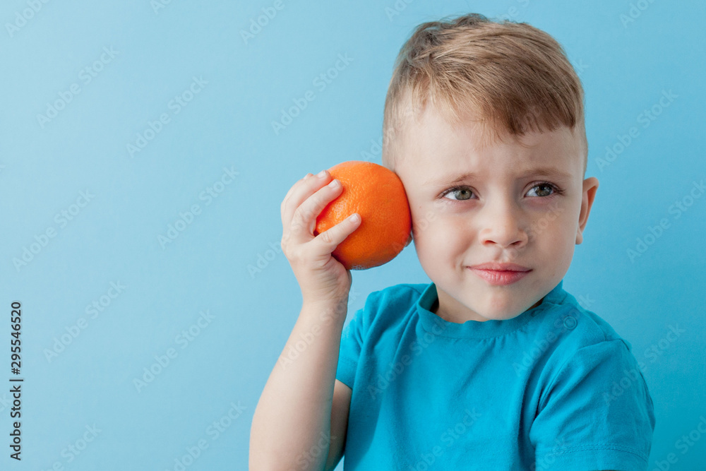 Little Boy Holding an Orange in his hands on blue background, diet and exercise for good health concept