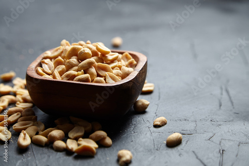 Wooden bowl with roasted peeled peanuts, salty beer snack on dark background photo