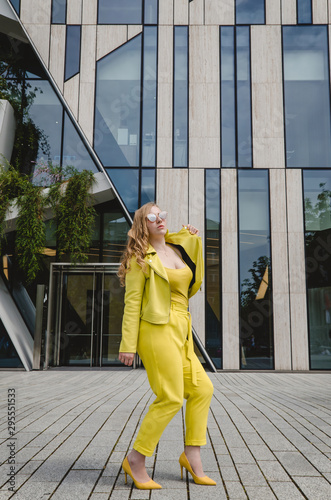 A young girl in a yellow suit is having fun dancing in the city center. Handsome and cheerful woman in black glasses. Girl traveling abroad on weekend getaway.