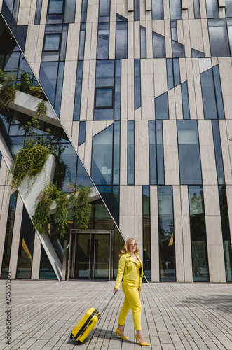 Young overjoyed traveler tourist woman in yellow summer yellow casual clothes. Girl traveling abroad on weekend getaway. Woman is dressed in yellow shoes with a yellow suitcase and black glasses.