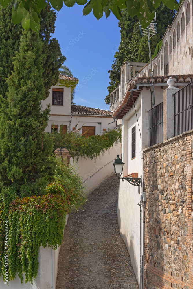 A small narrow street with white houses and abundant greenery in the old European city