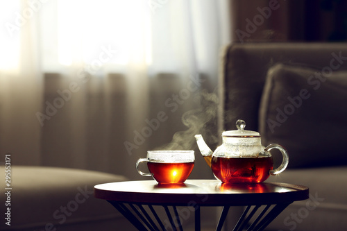 Teapot and cup of fresh hot tea on table against blurred background. Space for text