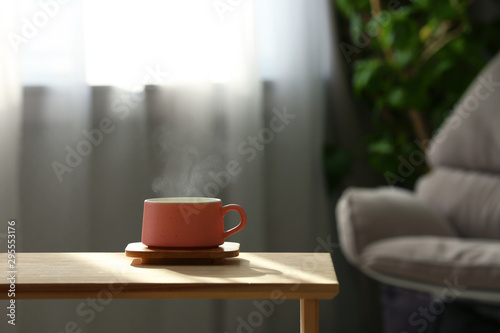 Cup with hot drink on wooden table against blurred background. Space for text