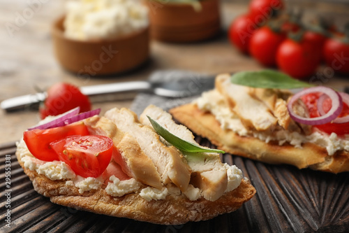 Board with delicious chicken bruschettas on table, closeup