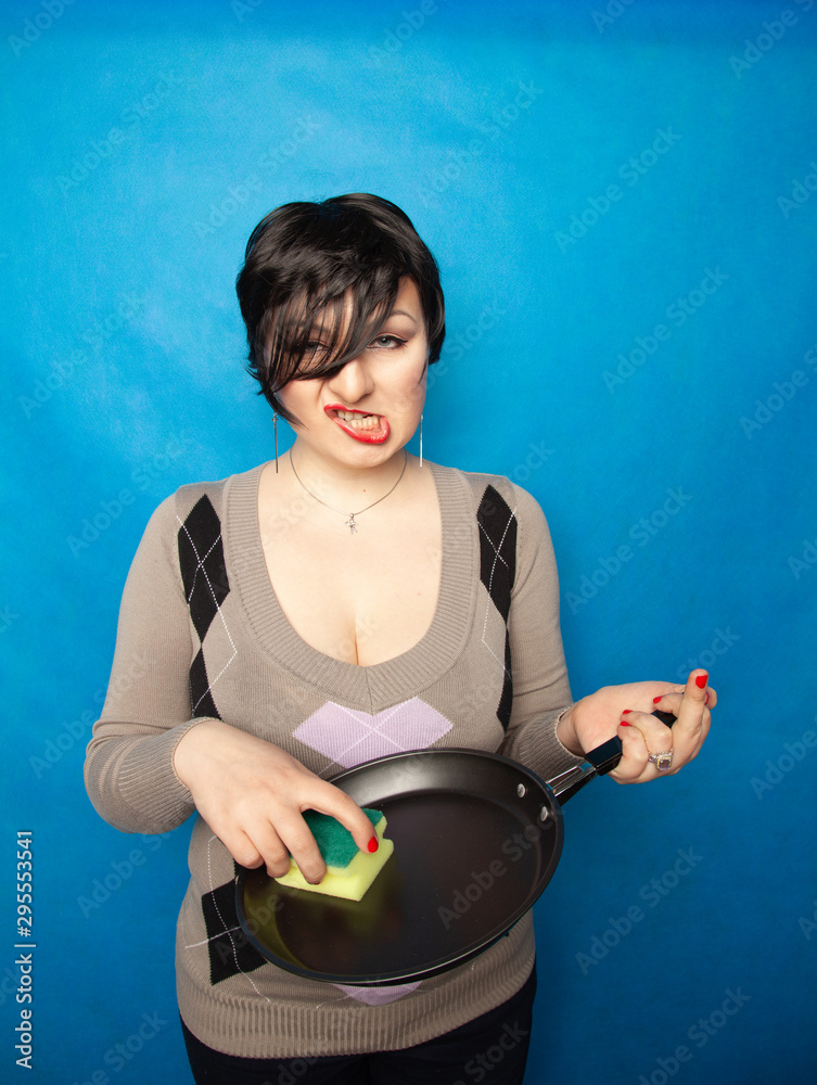 Cleaning dishware kitchen sink sponge washing frying pan. Housewife woman posing on blue studio background with skillet. Cleaning dishware kitchen sink sponge washing frying pan. Housewife woman posing on blue studio background with skillet.