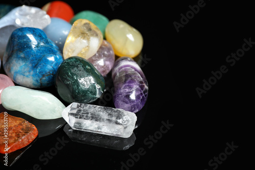 Different beautiful gemstones on black background, closeup. Space for text