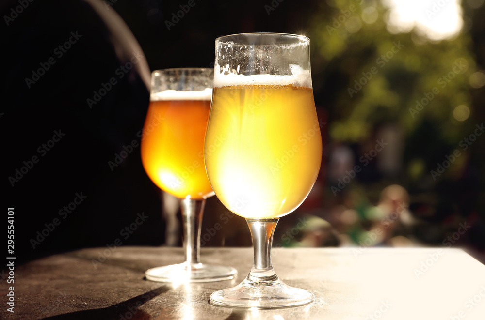 Glasses of cold tasty beer on wooden table outdoors