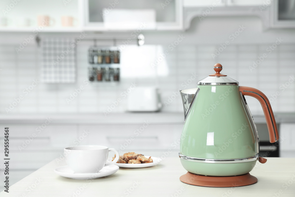 Modern electric kettle, cup and cookies on wooden table in kitchen Modern electric kettle, cup and cookies on wooden table in kitchen