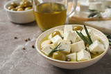 Composition with pickled feta cheese in bowl on light brown table