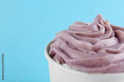 Cup with tasty frozen yogurt on light blue background, closeup. Space for text