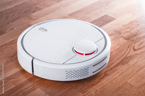white robotic vacuum cleaner in rays of morning sun. robot controlled by voice commands for direct cleaning. modern smart appliance for cleaning house