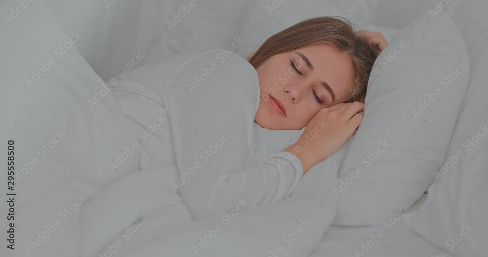 Beautiful girl lies under a white blanket in the bedroom and sleeps soundly. Portrait view. Beautiful girl lies under a white blanket in the bedroom and sleeps soundly. Portrait view.