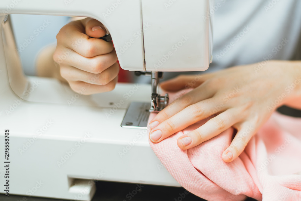 Seamstress works on a sewing machine. The girl sews and holds a pink cloth