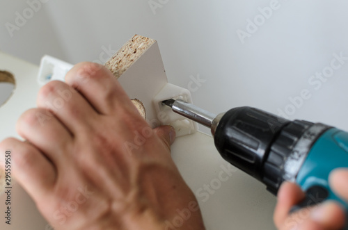 man hand fastens detail when assembling white furniture photo