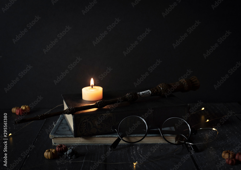 Fototapeta premium magic wand and spell books on desk with glasses, burning candle, and other witch items, wizards desk, halloween theme, vintage books