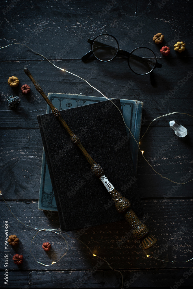 Fototapeta premium magic wand and spell books on desk with glasses and other witch items, wizards desk, halloween theme, vintage books