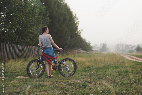 white caucasian young woman in casual clothing standing with bicycle, looking on town in evening fog, view from back in full body size, lifestyles stock photo image