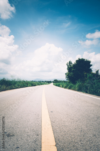 A long concrete road with a scene of mountains and grasslands beside the road.