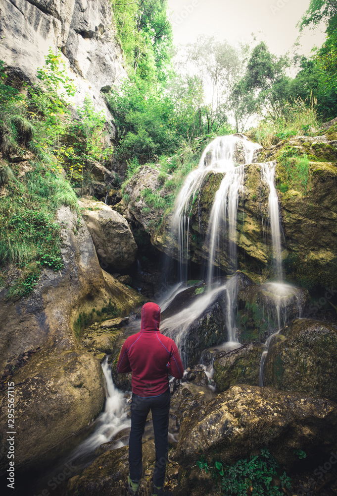 Hiker standing in front of a waterfall surrounded by rocks in the forest in austria Hiker standing in front of a waterfall surrounded by rocks in the forest in austria