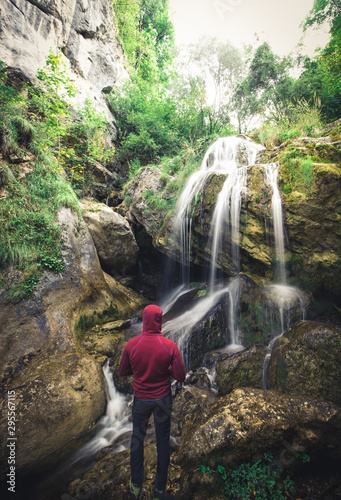 Hiker standing in front of a waterfall surrounded by rocks in the forest in austria
