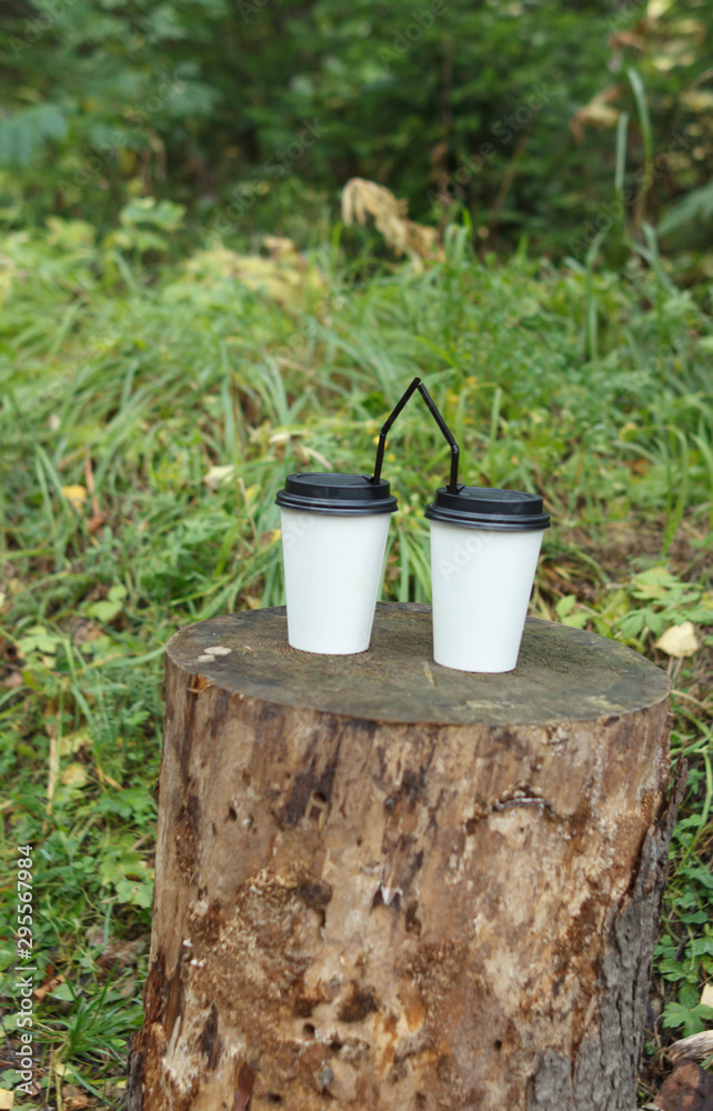 two paper cups for hot drinks with a straw on a wooden stump
