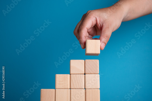 Hand arranging block on blue background. Business concept on progress or building something.