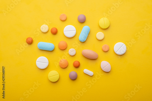 Top view colorful medical pills on yellow background.