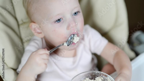 little girl ineptly eats porridge with a spoon. Close-up photo