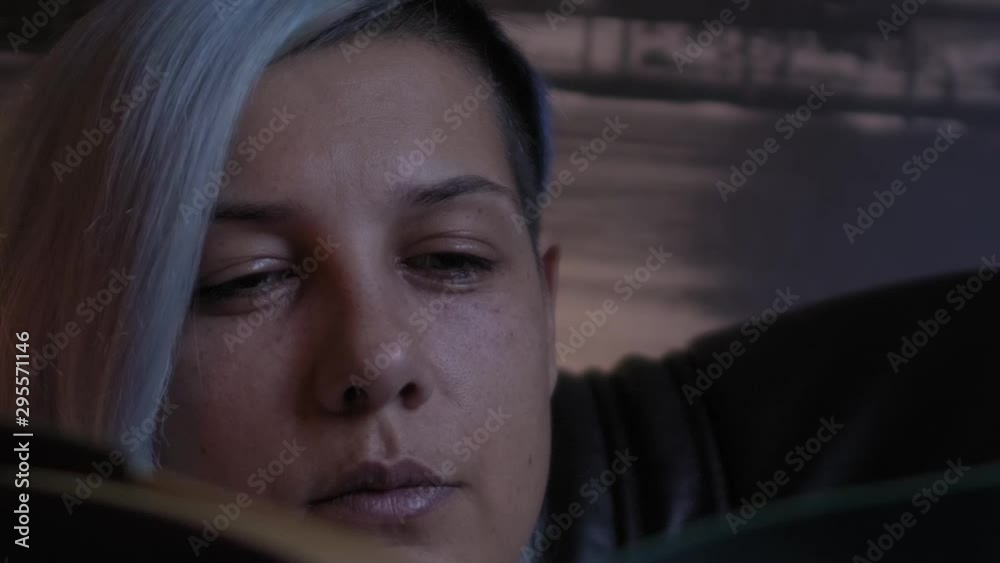 Young woman relaxing and reading an old book in dark and cozy room; with blue hair; close up. Young woman relaxing and reading an old book in dark and cozy room; with blue hair; close up.