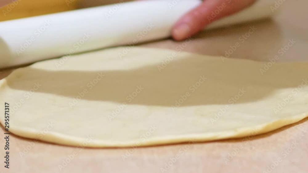 Woman using white rolling pin to roll raw dough into a circle; dinner rolls; slow motion. Woman using white rolling pin to roll raw dough into a circle; dinner rolls; slow motion.