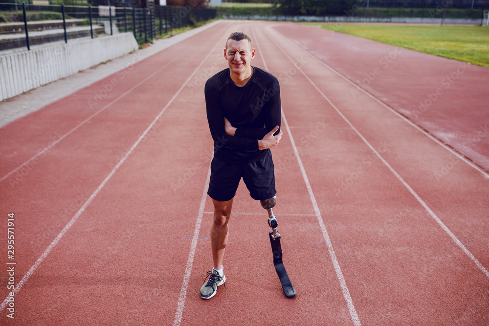 Sporty man with artificial leg standing on running track and having pain in stomach.