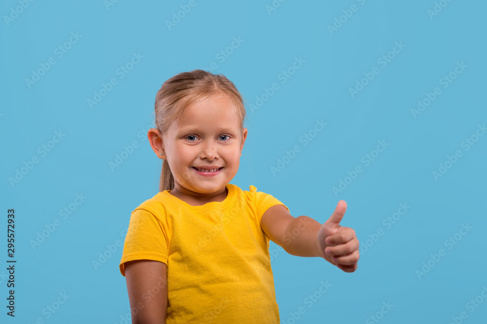 a little smiling girl giving you an approving gesture against blue background with copy space a little smiling girl giving you an approving gesture against blue background with copy space