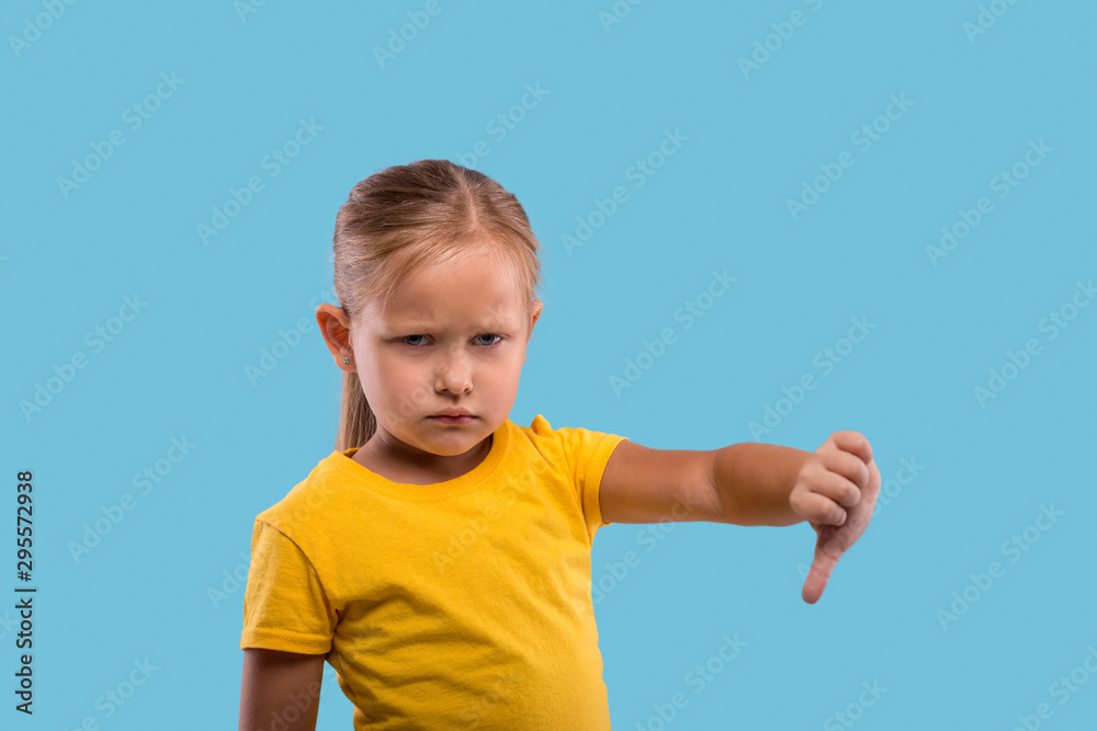 A little serious girl   showing a gesture everything is bad against  blue background in studio