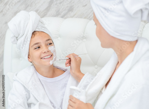 Mom puts white cream on her smiling daughter's face at home