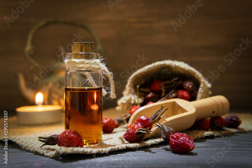 Rosehip oil on wooden background with red fruits