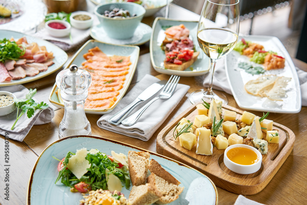 Various snacks and antipasti on the table. Restaurant menu. Cheese plate. Focus on delicious cheese mix with walnuts, honey on wooden table. Various snacks and antipasti on the table. Restaurant menu. Cheese plate. Focus on delicious cheese mix with walnuts, honey on wooden table.