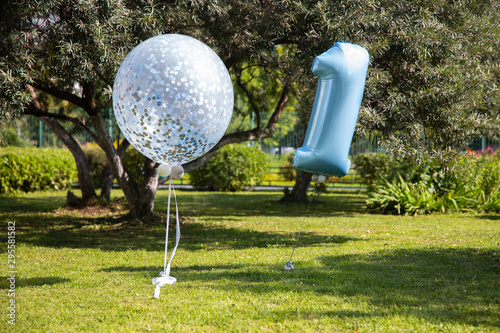 Balloons: big blue and number one on the big green glade in the garden, birthday