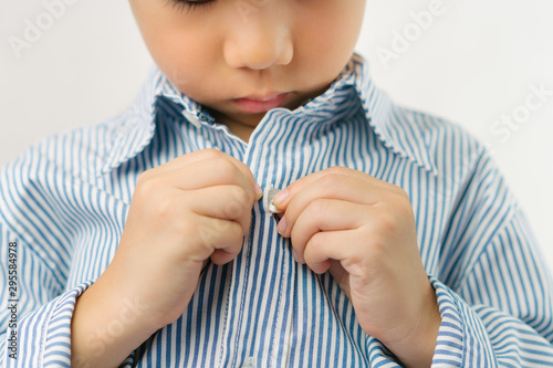 Child Development concept: Close up of a little kindergarten boy's hands learning to get dressed, buttoning his striped blue shirt. Montessori practical life skills - Care of self, Early Education.