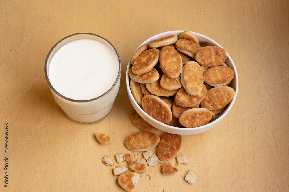 Fat cookies in a bowl, glass cup with milk, light brown wooden background. Fat cookies in a bowl, glass cup with milk, light brown wooden background.
