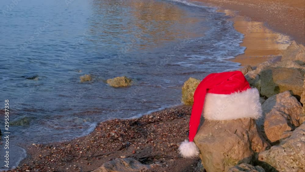 Christmas Santa Claus hat on tropical sandy beach with calm waves. Winter holidays. New Year celebration on island. Concept Christmas Santa Claus hat on tropical sandy beach with calm waves. Winter holidays. New Year celebration on island. Concept