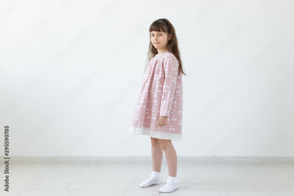 Little proud brunette girl in a pink dress is standing on a white background. The concept of stylish children's clothing and preschool age. Copyspace. Little proud brunette girl in a pink dress is standing on a white background. The concept of stylish children's clothing and preschool age. Copyspace.